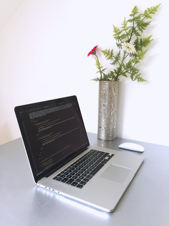 Laptop with programming code on screen beside a vase with flowers, creating a modern workspace.